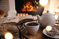 Cup of tea, cookies and book near fireplace indoors. Cozy atmosphere Royalty Free Stock Photo