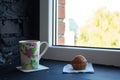 A cup with tea and cupcake near the window