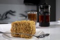 cup of tea in a double-botoom glass, french-press teapot and piece of cake on white table in gray kitchen