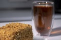 Cup of tea in a double-botoom glass and piece of cake on white table in gray kitchen