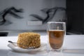 Cup of tea in a double-botoom glass and piece of cake on white table in gray kitchen