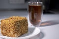 Cup of tea in a double-botoom glass and piece of cake on white table in gray kitchen