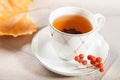 A cup of tea with falling autumn leaves of maple, and a bunch of rowan