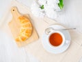 Cup of tea, flowers and fresh baked puff pastry on a white table. Delicious croissants on wooden board, top view