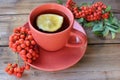 Cup of tea with lemon and red rowan berries on wooden table. Cozy autumn composition