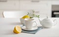 A cup of tea with lemon and a teapot on a white table against the background of a white kitchen Royalty Free Stock Photo