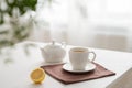 A cup of tea with lemon and a teapot on a white table with green branch against the background of a kitchen window Royalty Free Stock Photo