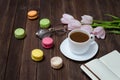 Cup of tea, macarons, glasses, pink tulips and notebook on wooden background.