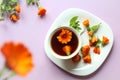 A Cup of tea with marigold flowers in a white dish with scattered flowers, purple background, top view, bokeh - the concept of