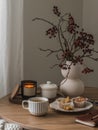 Cup of tea, muffins, cranberry branches in a vase, a notebook, a burning candle on a round wooden table in the living room