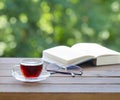 Cup of tea and open book on wooden table outdoors over beautiful green garden bokeh background Royalty Free Stock Photo