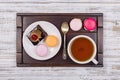 Cup of tea, piece chocolate cake and macaron cakes on tray on white wooden table. Lifestyle concept. Royalty Free Stock Photo