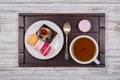 Cup of tea, piece chocolate cake and macaron cakes on tray on white wooden table. Lifestyle concept. Royalty Free Stock Photo