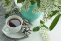 cup with tea on a saucer, a chocolate chip cookie towel and a vase with cherry branches on the windowsill