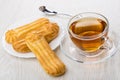 Cup with tea on saucer, spoon, eclairs in white plate