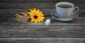 A cup of tea on a saucer and a spoon stand on a table with about two cupcakes on a napkin, a yellow bud and two cubes of sugar Royalty Free Stock Photo