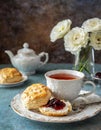 A cup of tea and scones with jam and cream.