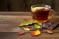 Cup of tea with slice of lemon and chocolate with autumn leaves on old wooden table.