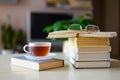 A cup of tea stands on a closed book next to a tall stack of books on the table at home. Royalty Free Stock Photo