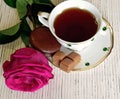 A Cup of tea is on the table, next to the saucer are sweets and cookies. Rose next to a Cup of tea. Royalty Free Stock Photo