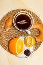 A cup of tea with a tea bag, a saucer with citrus fruits and candy, next to a bagel with poppy seeds. A pleasant tea party