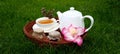 a cup of tea and a teapot on a wooden stand with a jar of honey and pink flowers