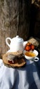 a cup of tea and a teapot on a wooden stand with jars of honey on a white tablecloth