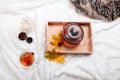 Cup of tea and teapot in wooden tray on the bed. Warm sweater, candles, yellow leaves. The concept of cozy autumn weekend house. Royalty Free Stock Photo