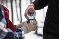 A cup of tea from a thermos on winter picnic in the woods. Woman hand`s in a warm gloves