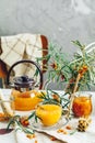Cup and teapot of hot spicy tea with sea buckthorn, jam in the glass jar, branches of fresh berries on light woden table surface Royalty Free Stock Photo