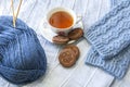 Cup of tee with chocolate cookies, knitted socks and ball of yarn with knitting needles