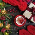 Cup of winter tea with decorated fir branches, cranberries, red mittens, hat, Christmas present with empty tag and plaid blanket o Royalty Free Stock Photo