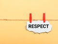Cupboard strip written respect hanging on clothes line against yellow background.