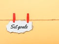 Cupboard strip written set goals hanging on clothes line against yellow background. Ambition concept