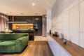 Cupboard with vases and clock in modern elegant living room interior with green velvet sofa and dark kitchen corner