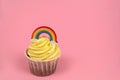 cupcake decorated with rainbow figurine on a pastel pink background