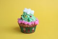 A cupcake with a lot of cream and decorated with a snowflake stands on a yellow background.