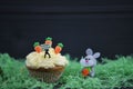 Cupcake topped with a miniature person figurine holding a sign for happy Easter with decorations of a bunny rabbit and carrots Royalty Free Stock Photo