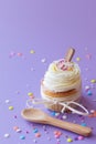 Cupcake with white frosting and sprinkles, wooden spoon on purple background Royalty Free Stock Photo