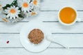 A cupcake on a white plate, a cup of green tea, a bunch of daisy flowers.