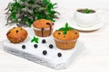 Cupcakes with black currants on a white wooden cutting board against the background of a cup and mint flowers. Royalty Free Stock Photo