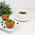 Cupcakes with black currants on a white wooden cutting board against the background of a cup and mint flowers. Royalty Free Stock Photo