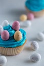 Cupcakes with blue icing with candy easter eggs on a white marble worktop