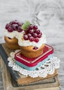 Cupcakes with cream and red currants on a light wooden background