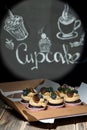 Cupcakes with fruits and berries in a box on a wooden table, a wall with chalk drawings, different light effects
