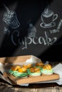 Cupcakes with fruits and berries in a box on a wooden table, a wall with chalk drawings, different light effects
