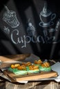 Cupcakes with fruits and berries in a box on a wooden table, a wall with chalk drawings, different light effects