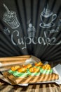 Cupcakes with fruits and berries in a box on a wooden table, a wall with chalk drawings, different light effects