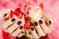 Cupped hands with dark manicure holding red flowers