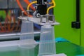 Cups on conveyor belt of plastic injection molding machine with robotic arm